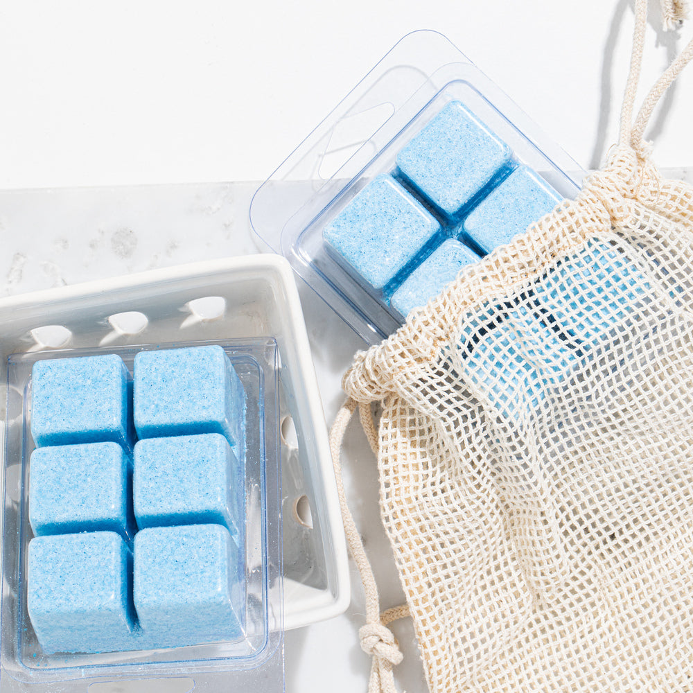 Blue toilet cleaning tabs in plastic clamshell packages beside mesh drawstring bag on white bathroom surface