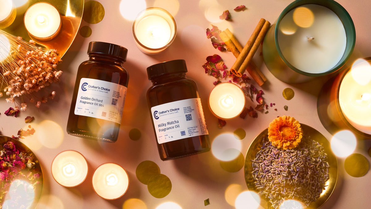 Two Crafter’s Choice fragrance oil bottles surrounded by glowing candles, dried flowers, cinnamon sticks, herbs, and colorful botanicals in warm golden light.