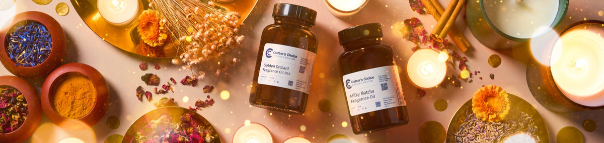 Two Crafter’s Choice fragrance oil bottles surrounded by glowing candles, dried flowers, cinnamon sticks, herbs, and colorful botanicals in warm golden light.