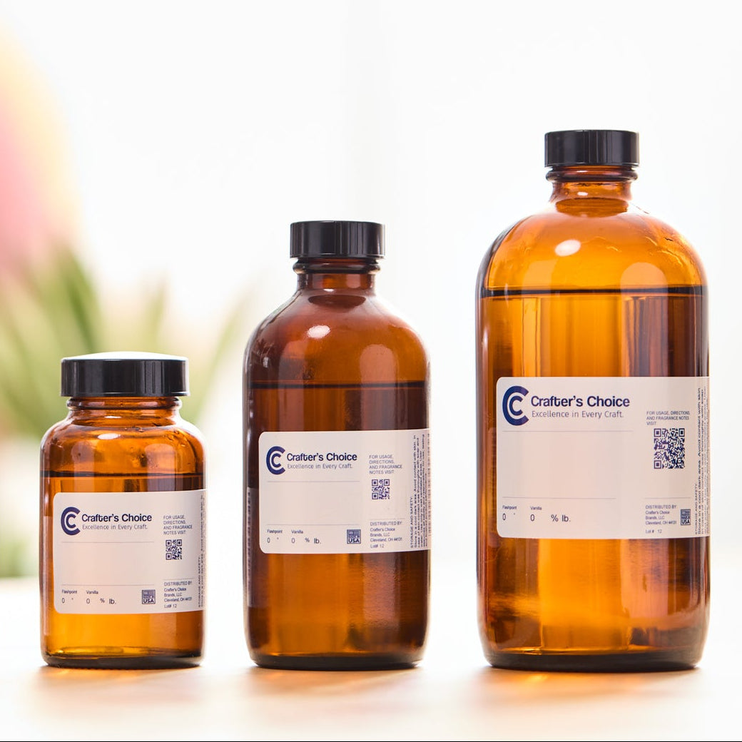 Row of amber glass fragrance oil bottles in multiple sizes with black caps, arranged on a light wooden surface against a softly blurred studio background.