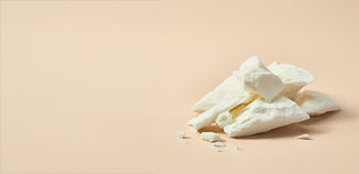 Irregular pieces of creamy white solid butter or wax piled on a warm beige background.