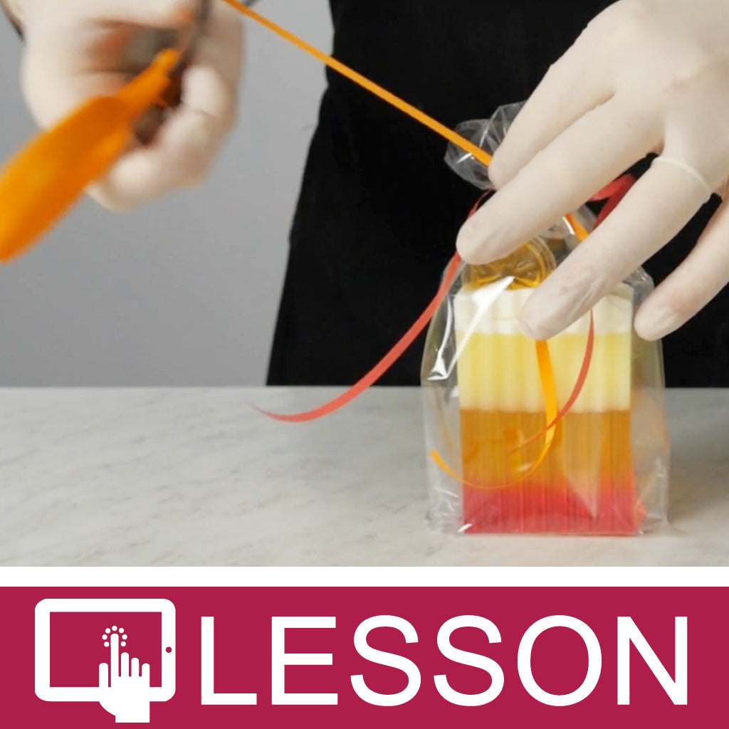Gloved hands tying ribbon around layered melt and pour soap in a clear bag