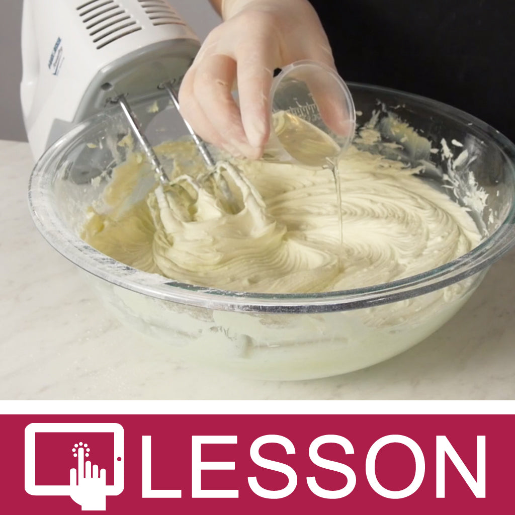 Gloved hand adding oil to whipped body butter beside a hand mixer