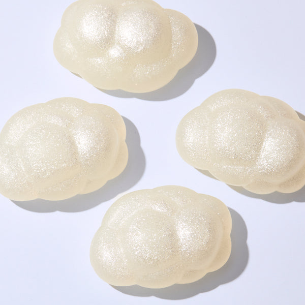 Four pearlescent white cloud-shaped bars arranged on a clean white background, photographed from above with soft shadows highlighting their shimmering finish.