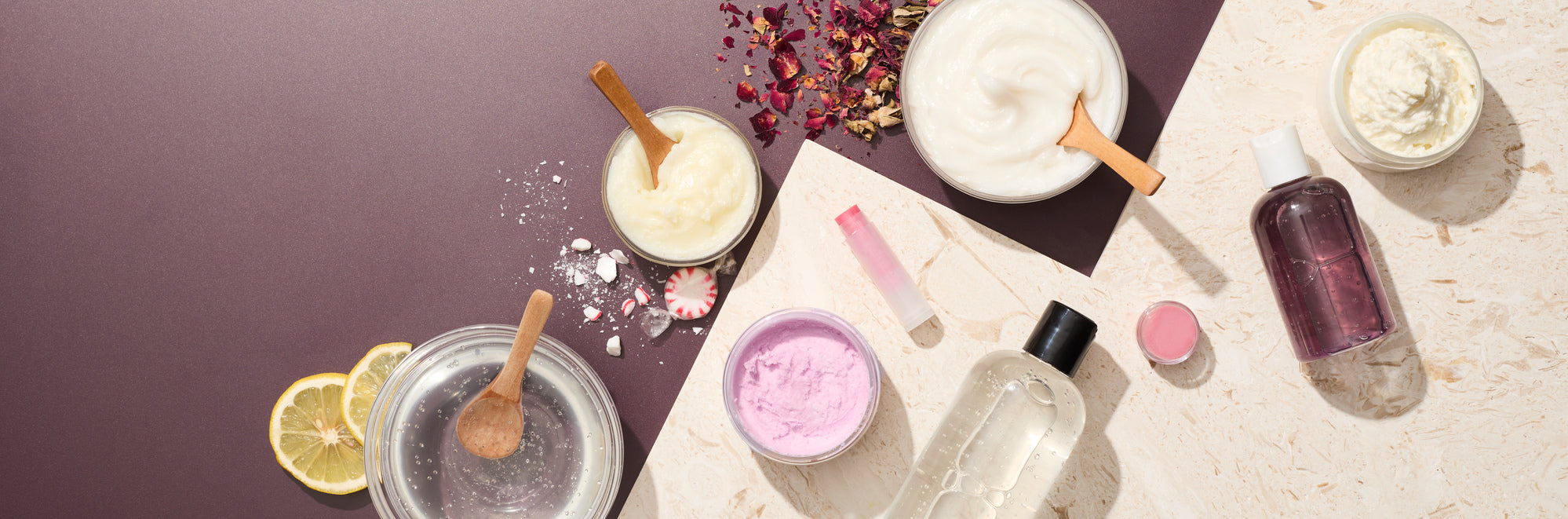 Flat lay of handmade beauty and personal care products on a neutral background, including jars of creams and scrubs, lip balm, bottles, wooden spoons, dried botanicals, lemon slices, and pastel textures arranged in a clean, modern layout.