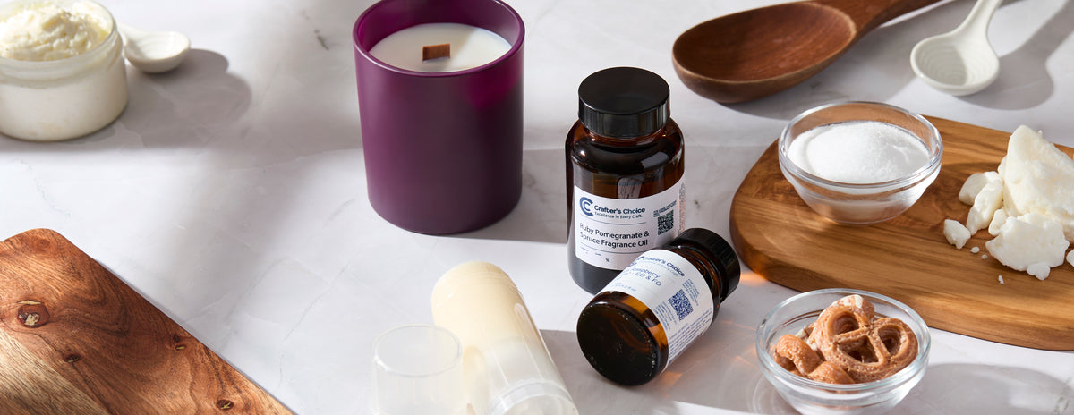 Crafter’s Choice fragrance oils, a purple jar candle, whipped body butter, and bath and body ingredients arranged on a marble surface.